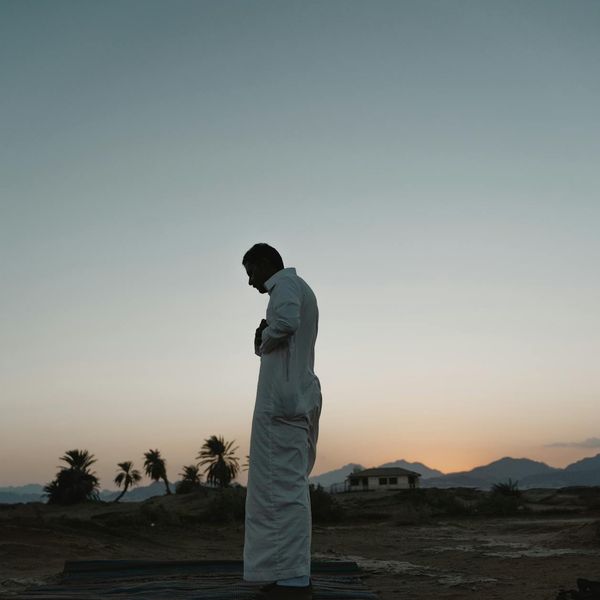 Person looking serene and content while stretching outdoors during sunrise.
